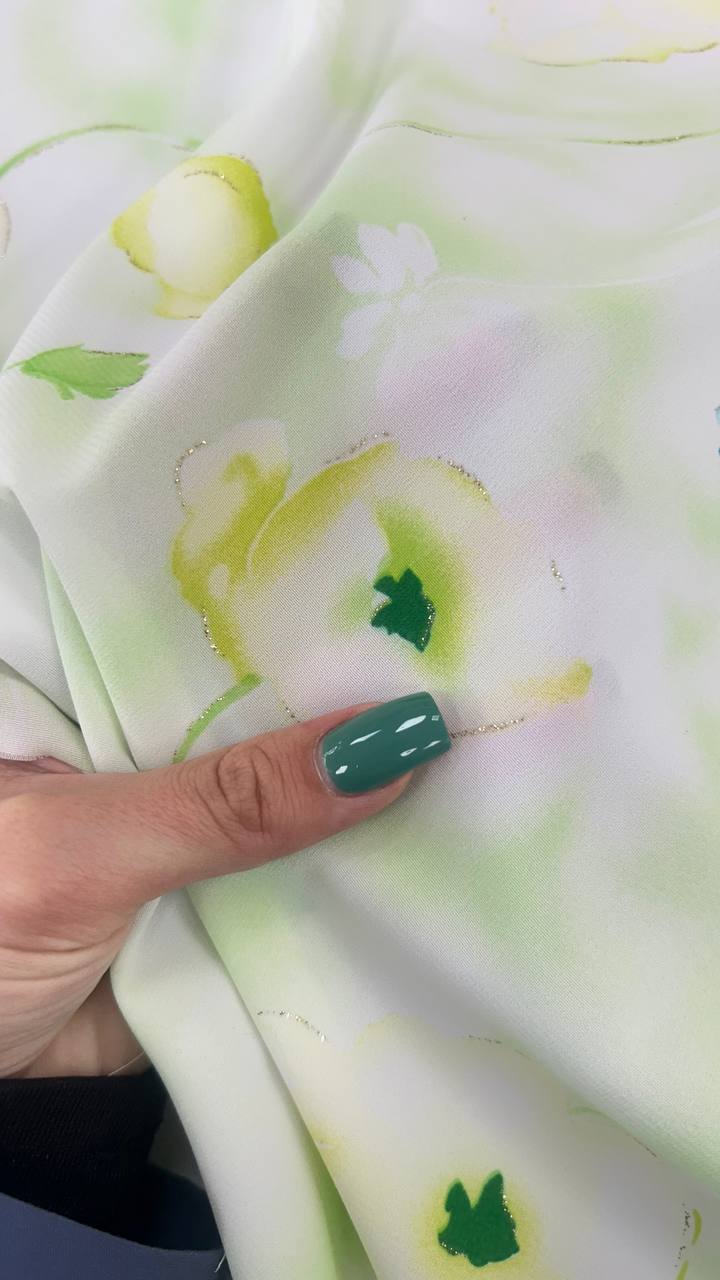 Close-up of pastel floral fabric being held by a hand with teal nail polish, featuring soft green and yellow flowers.