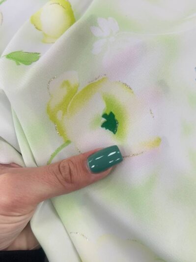 Close-up of pastel floral fabric being held by a hand with teal nail polish, featuring soft green and yellow flowers.